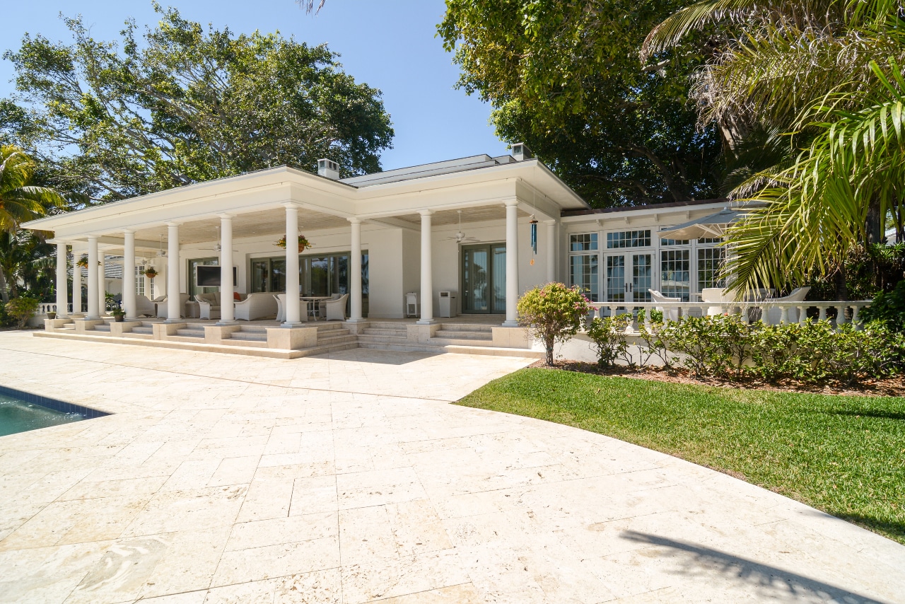 Beige home with columns and beige stone paver walkway around pool.